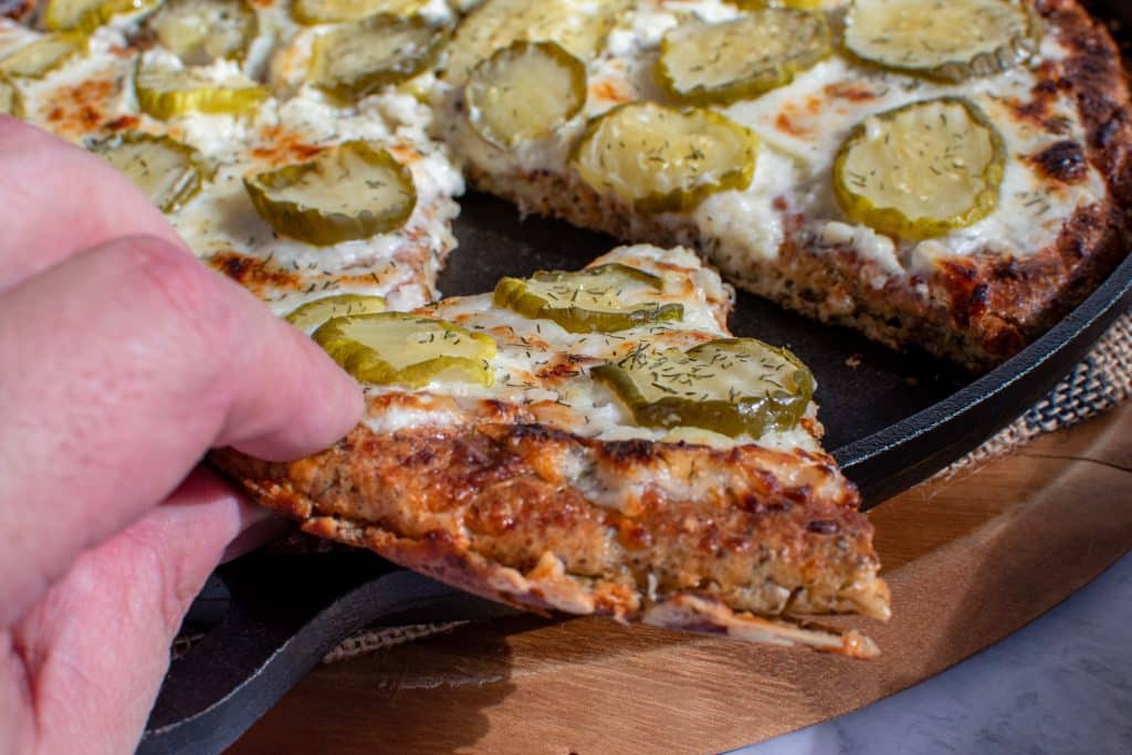 grabbing a slice of low carb dill pickle pizza from cast iron skillet