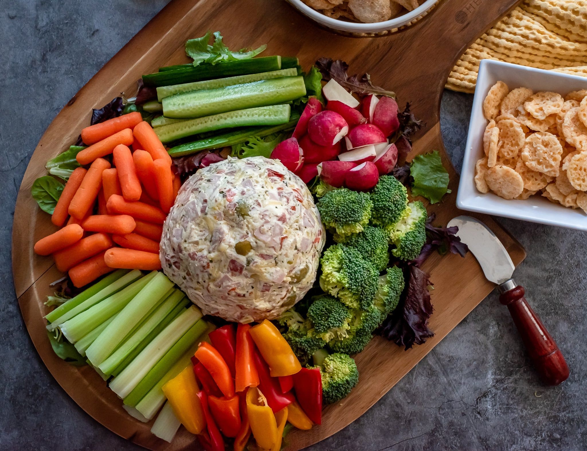 Muffuletta dip served on a pizza peel with veggies and pork rinds