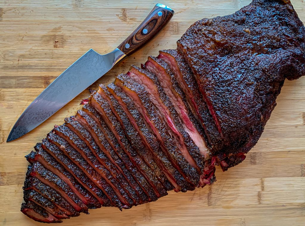 Sliced Texas brisket on wood cutting board with chef knife