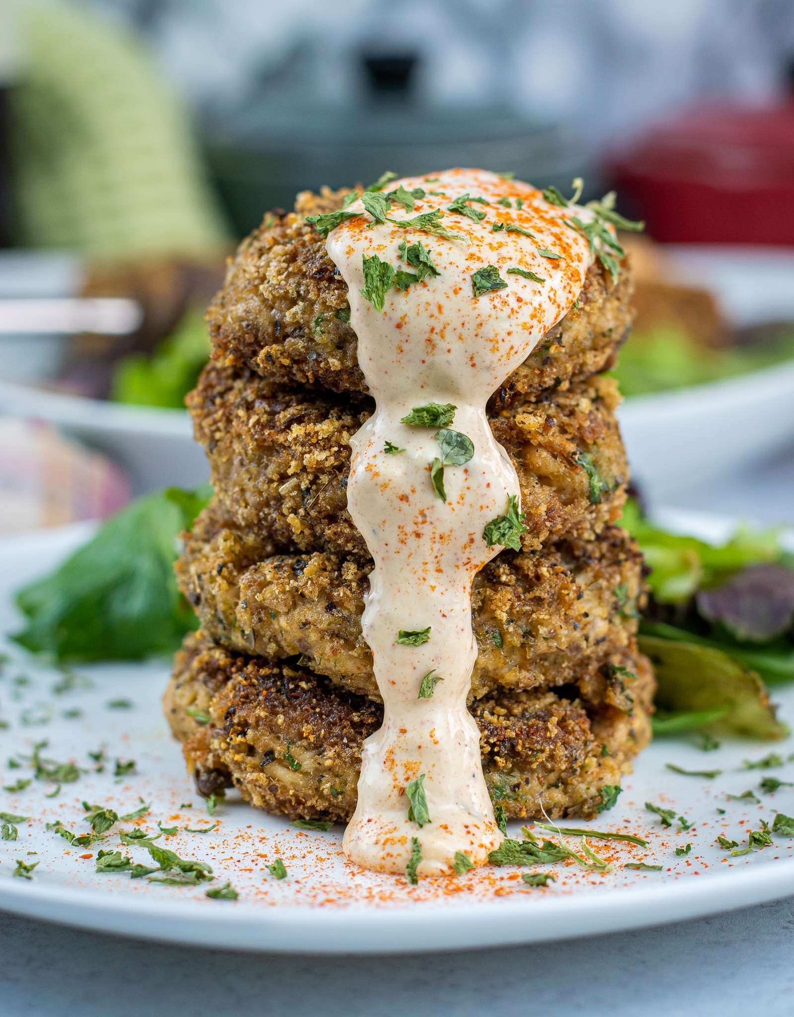 pouring spicy lemon caper aioli over crispy piccata fish cakes