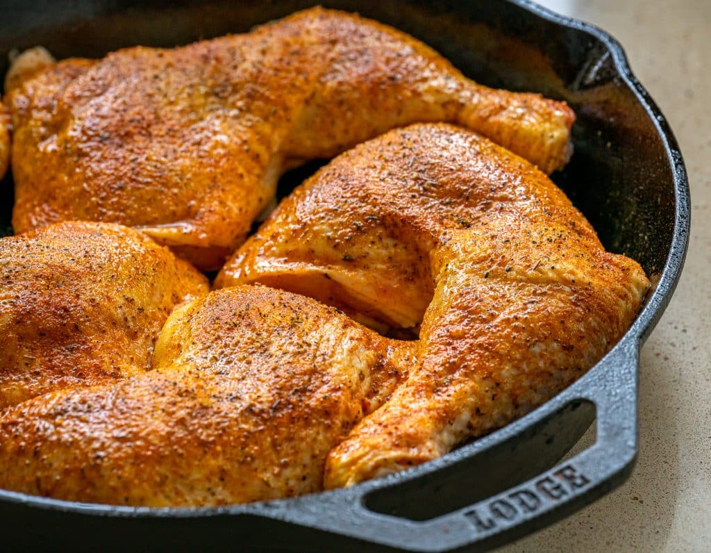 uncooked chicken leg quarters in a cast iron skillet with lemon pepper seasoning