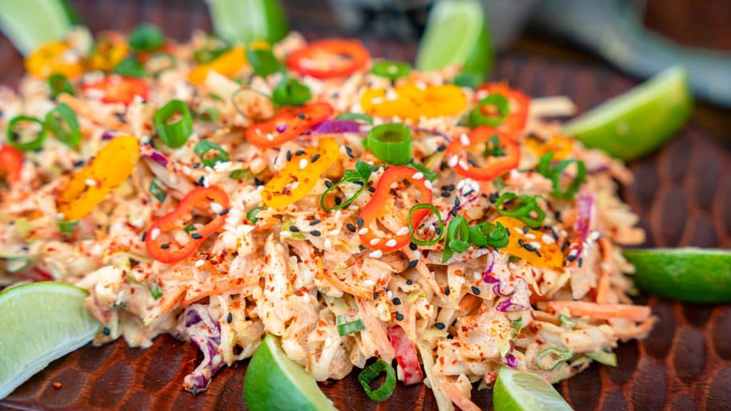 kimchi coleslaw garnished with sesame seeds, chili flakes and lime wedges