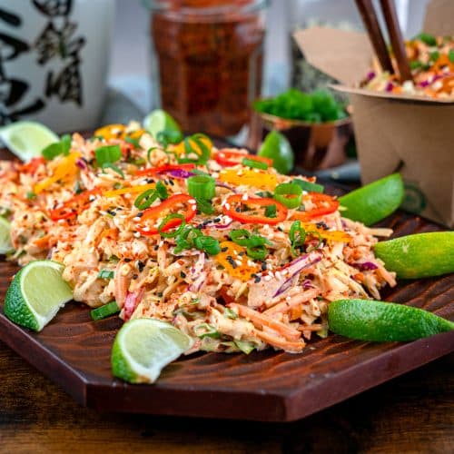 kimchi coleslaw garnished with sesame seeds, chili flakes and lime wedges