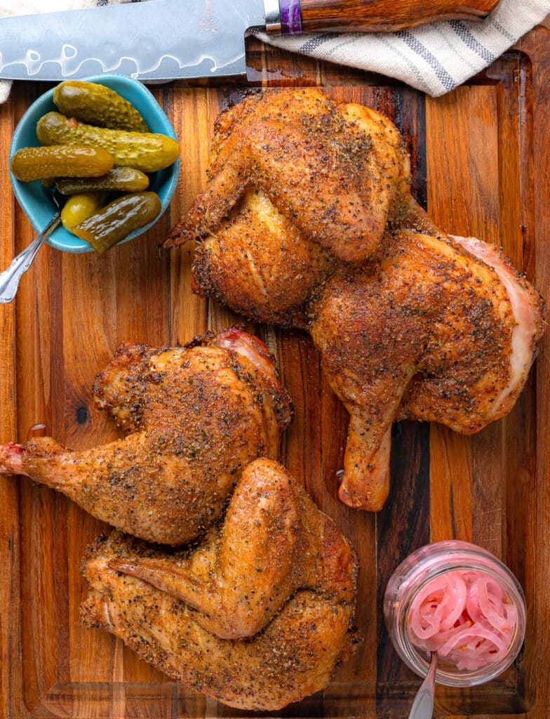 smoked half chicken on a teak wood cutting board with onions and pickles