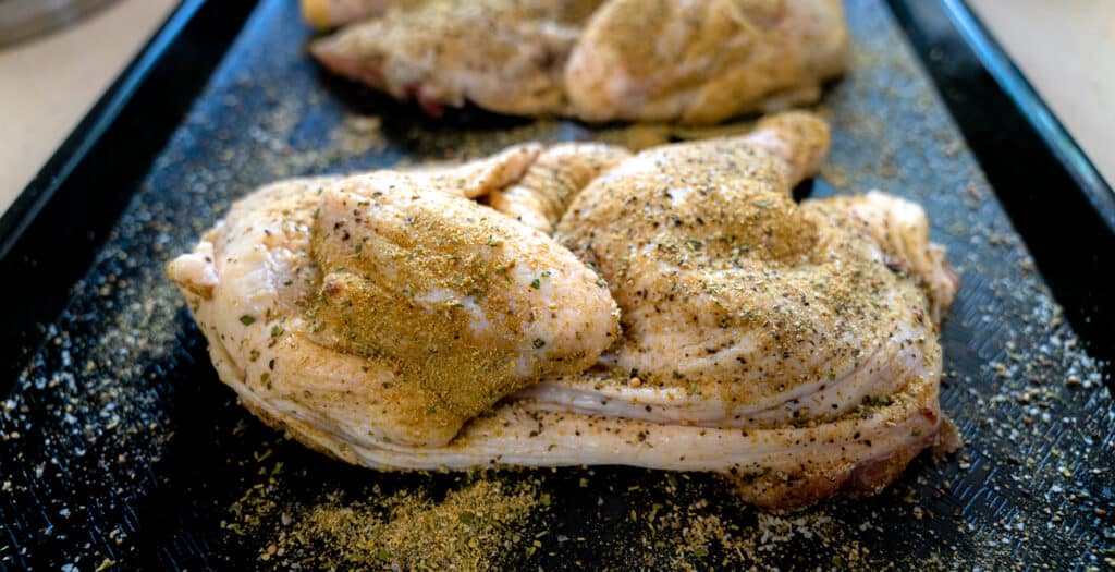 raw chicken cut in half seasoned with salt and pepper blend
